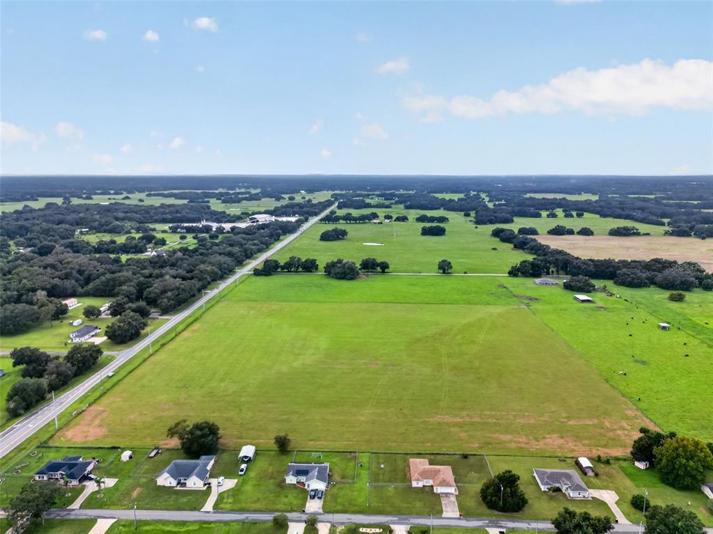 An aerial view shows a large, open green pasture bordered by a road and houses — TBD WC 48, BUSHNELL, FL