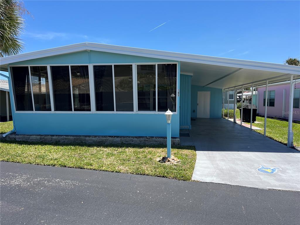 A light blue mobile home features a large screened-in porch and an attached covered carport — 165 LOOKOUT DRIVE, FLAGLER BEACH, FL