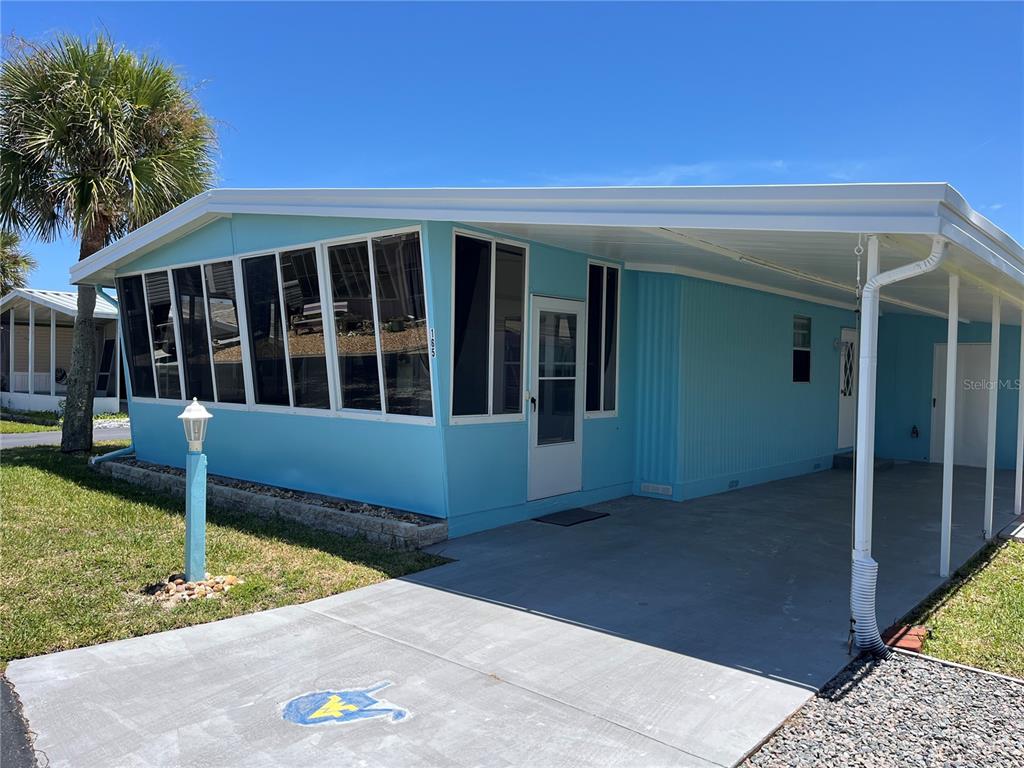 A light blue mobile home features a large screened-in porch and an attached concrete carport — 165 LOOKOUT DRIVE, FLAGLER BEACH, FL