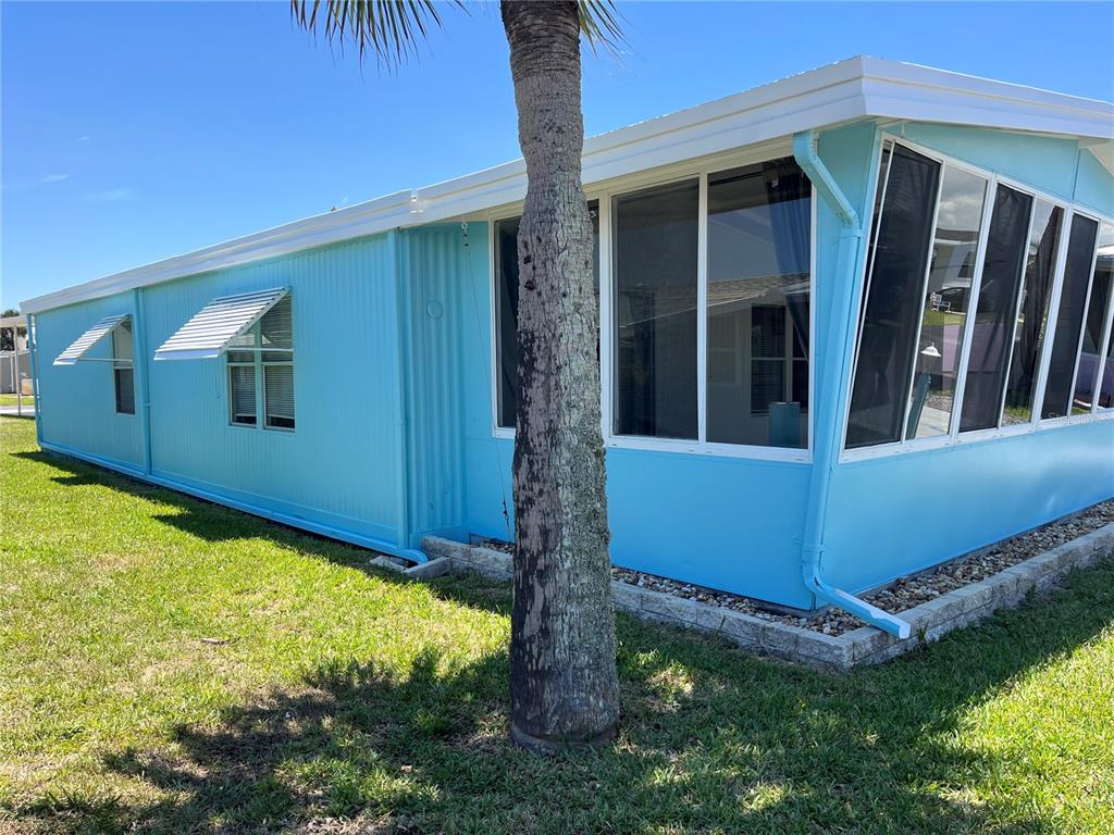 A bright blue mobile home exterior features a screened-in porch and a palm tree — 165 LOOKOUT DRIVE, FLAGLER BEACH, FL