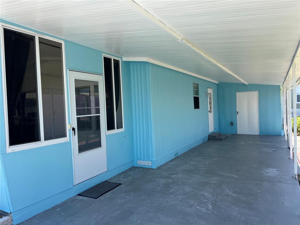 A light blue mobile home exterior features a covered concrete carport and two white doors — 165 LOOKOUT DRIVE, FLAGLER BEACH, FL