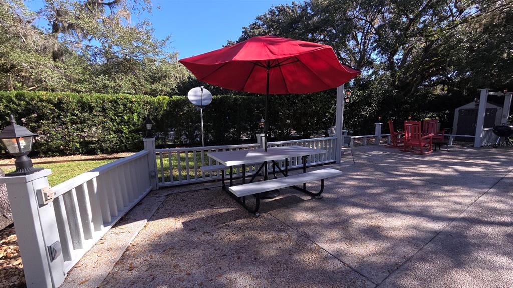 A concrete patio features a picnic table with a red umbrella and white railing — 376 BEAR TRAIL, RIVER RANCH, FL