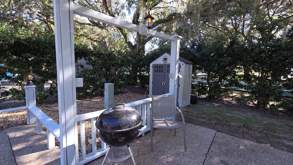 A patio features a charcoal grill, a chair, and a storage shed under large trees — 376 BEAR TRAIL, RIVER RANCH, FL