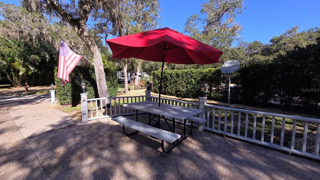 A red patio umbrella shades a picnic table on a concrete deck with white railings — 376 BEAR TRAIL, RIVER RANCH, FL