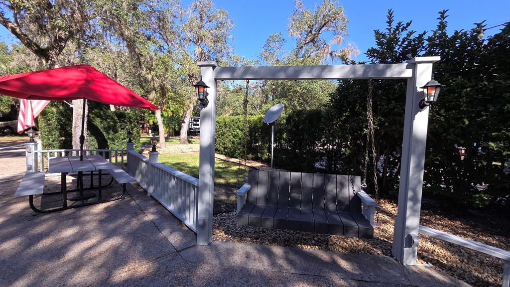 A patio features a picnic table with a red umbrella and a wooden porch swing — 376 BEAR TRAIL, RIVER RANCH, FL