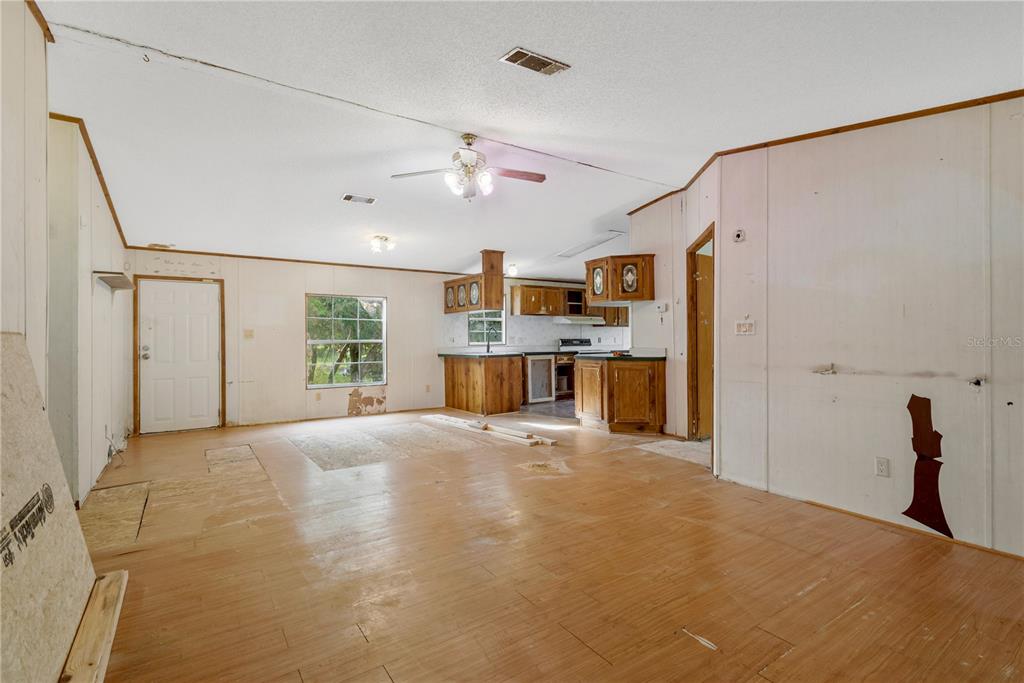 An open-concept living area with wood-look flooring, a kitchen, and unfinished wall panels — 11620 E BAY ROAD, GIBSONTON, FL