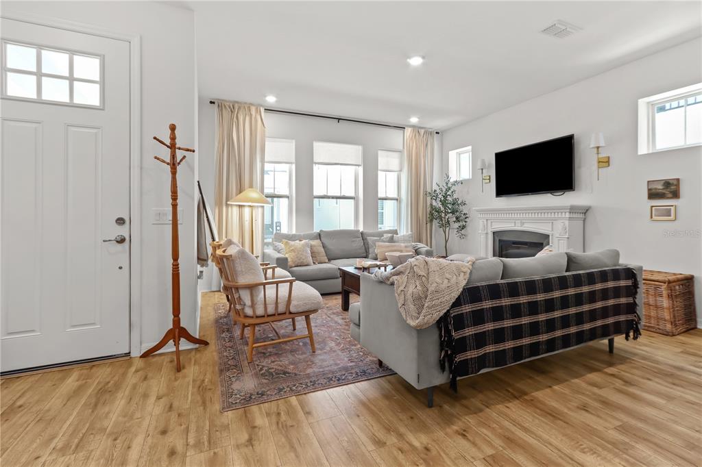 A living room features a fireplace, gray sofas, a patterned rug, and wood-look flooring — 923 COLIE ALLEY, WINTER GARDEN, FL