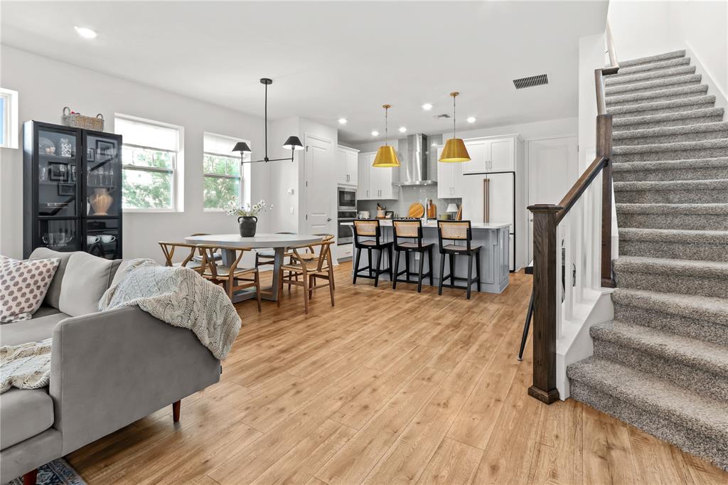 An open-concept kitchen, dining area, and living room feature light wood floors and carpeted stairs — 923 COLIE ALLEY, WINTER GARDEN, FL
