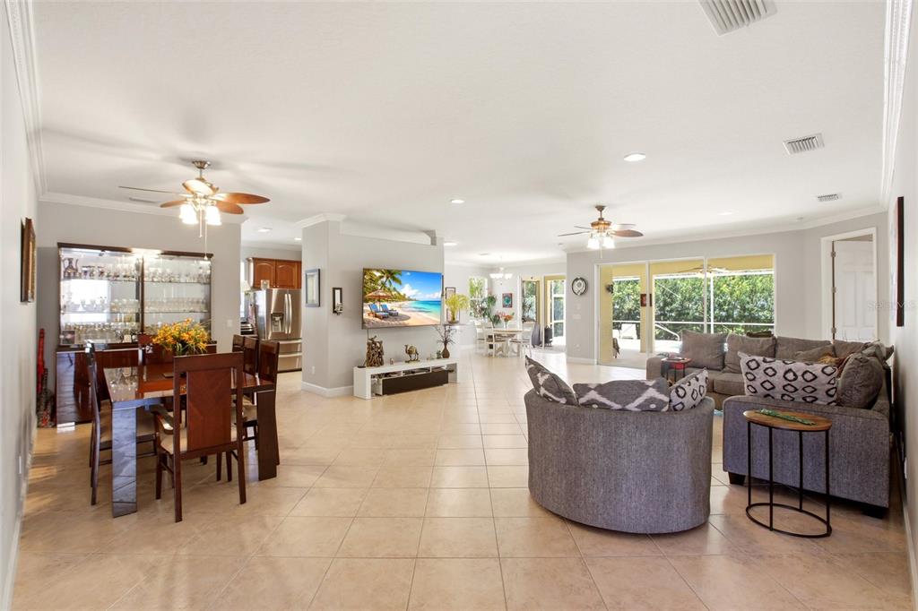 An open-concept living and dining area features tile flooring, ceiling fans, and a large television — 7131 67TH TER E, BRADENTON, FL