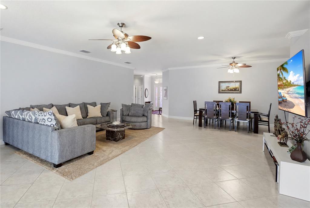 A spacious open-concept living and dining area with gray furniture, tile floors, and ceiling fans — 7131 67TH TER E, BRADENTON, FL