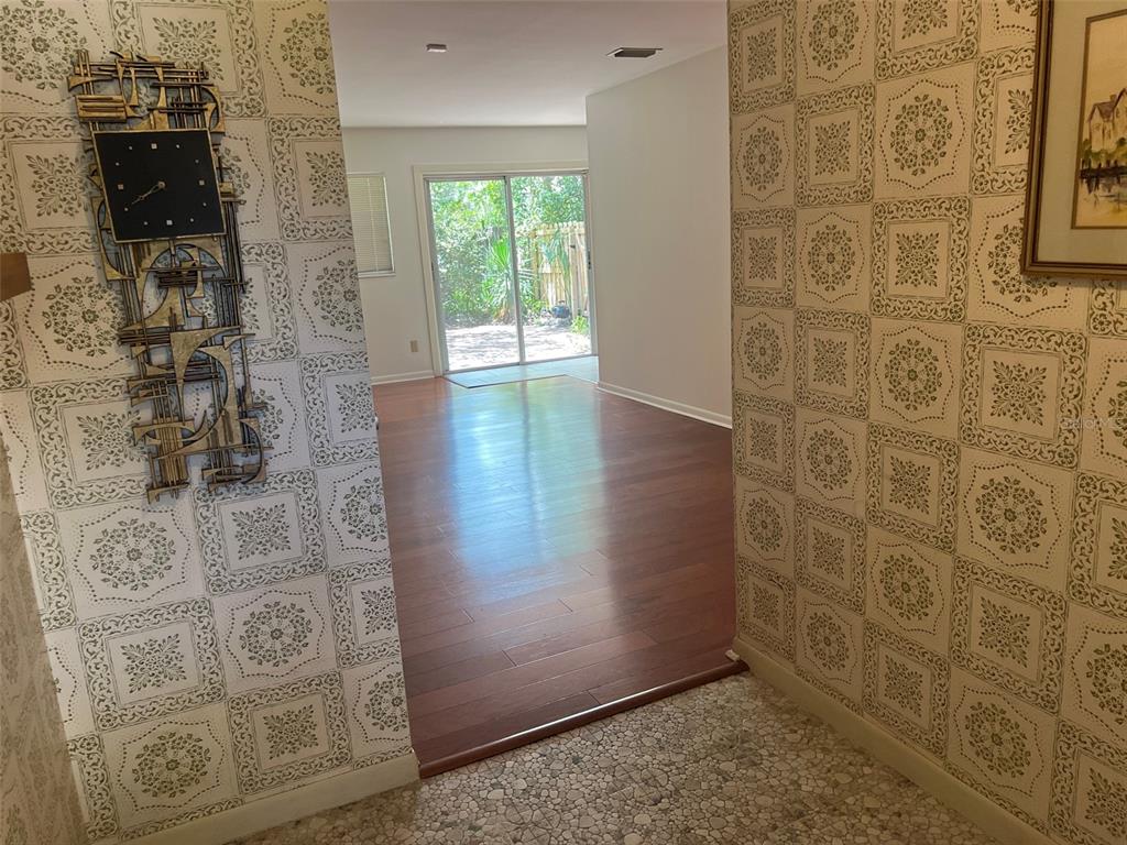 A hallway with patterned wallpaper and a wall clock leads to a room with hardwood floors — 703 NE 5TH PLACE, GAINESVILLE, FL