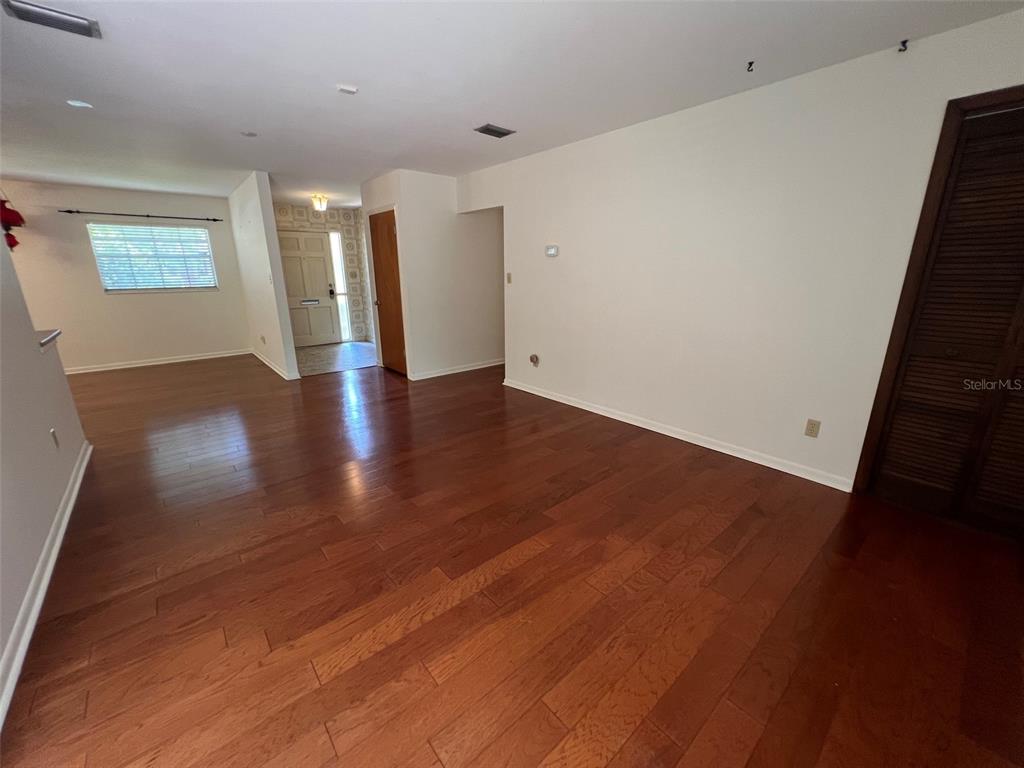 An empty living area features hardwood flooring, white walls, and a wooden closet door — 703 NE 5TH PLACE, GAINESVILLE, FL