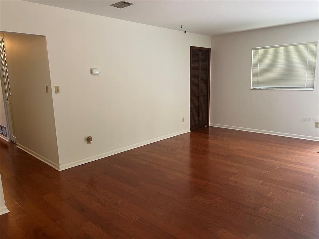 An empty room with hardwood floors, white walls, a window with blinds, and a closet door — 703 NE 5TH PLACE, GAINESVILLE, FL