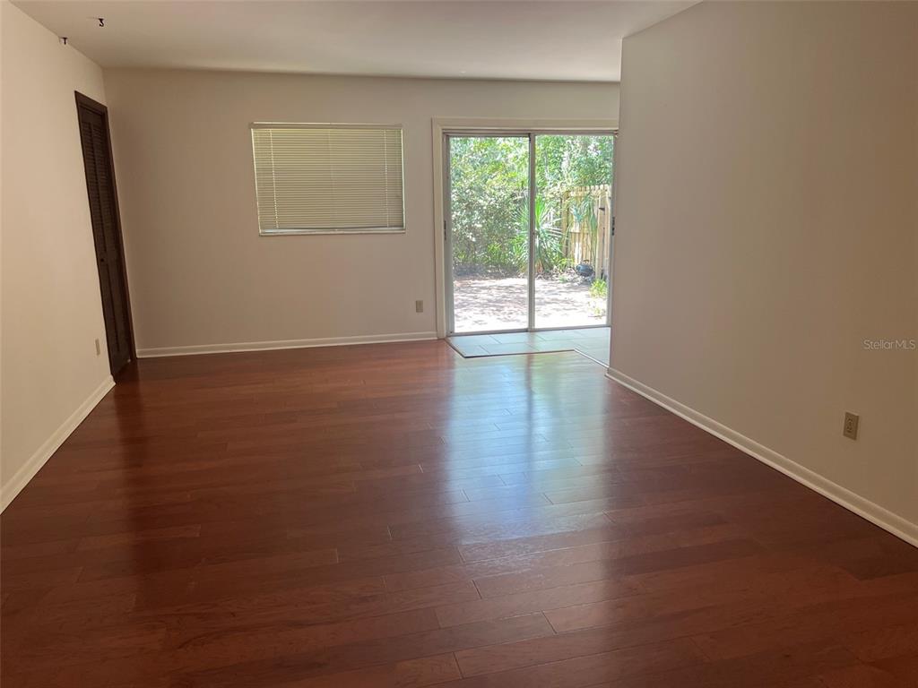 An empty living room features wood-look flooring, a sliding glass door, and a window with blinds — 703 NE 5TH PLACE, GAINESVILLE, FL