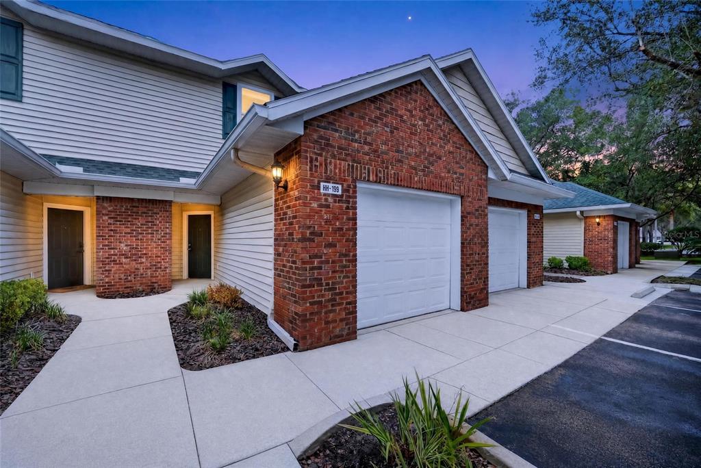 Exterior view of a multi-unit residential building with brick accents, white garage doors, and walkways — 13200 W NEWBERRY ROAD UNIT HH199, NEWBERRY, FL