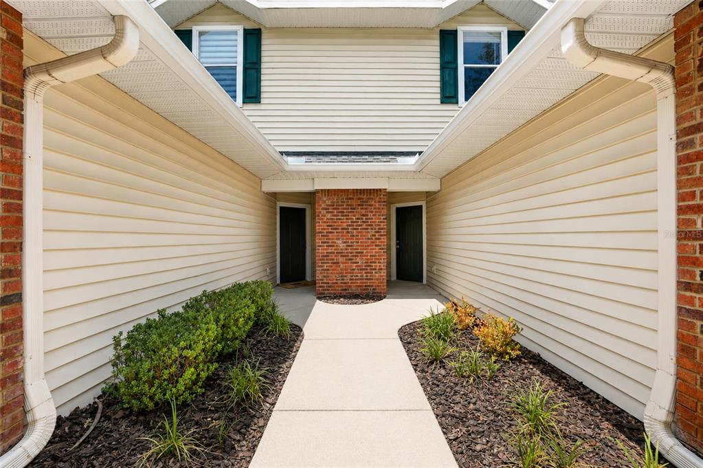 A concrete walkway leads to two dark front doors flanked by beige siding and brick — 13200 W NEWBERRY ROAD UNIT HH199, NEWBERRY, FL