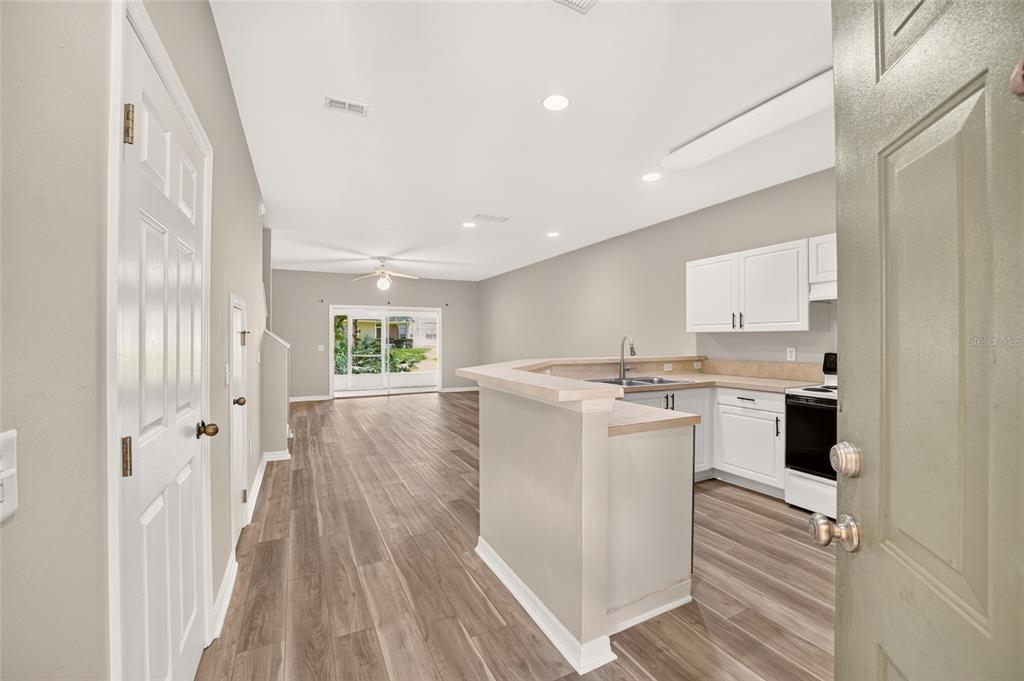 An open-concept kitchen and living area featuring wood-look flooring, white cabinets, and a breakfast bar — 13200 W NEWBERRY ROAD UNIT HH199, NEWBERRY, FL