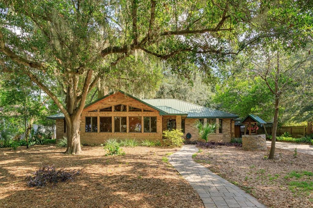 A single-story brick house with a green metal roof sits behind a stone walkway — 10350 LAKE LOUISA ROAD, CLERMONT, FL
