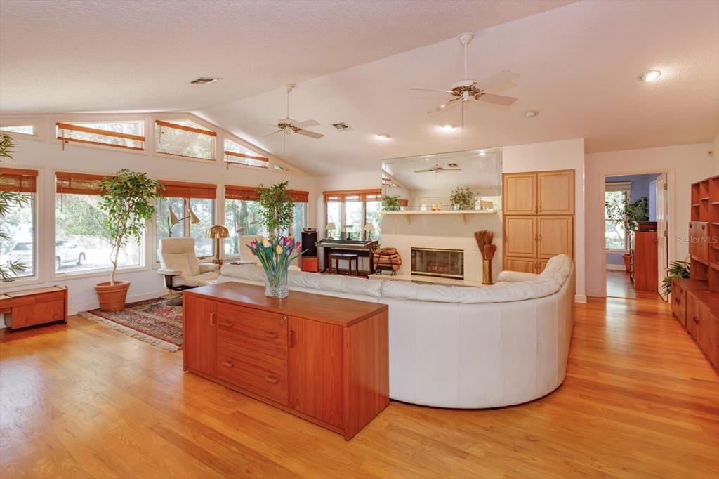 A spacious living room features a white curved sofa, hardwood floors, and a brick fireplace — 10350 LAKE LOUISA ROAD, CLERMONT, FL
