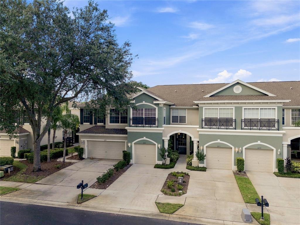 An exterior view of a multi-unit townhouse complex with green siding and attached garages — 2251 PARK CRESCENT DRIVE, LAND O LAKES, FL