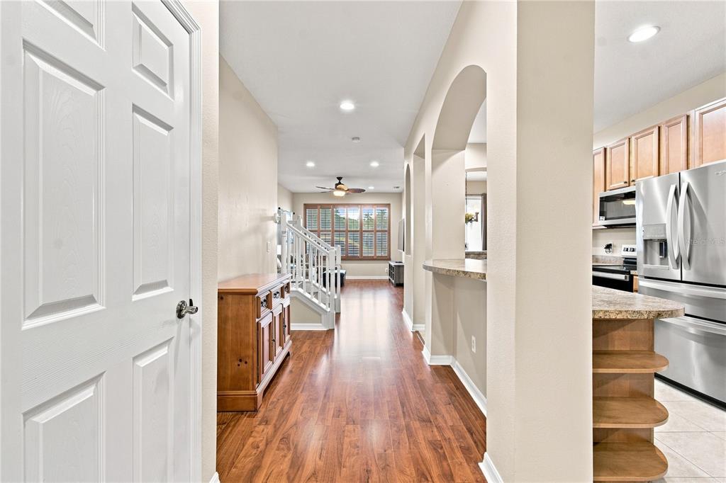 A hallway with wood flooring leads past a kitchen and staircase toward a living area — 2251 PARK CRESCENT DRIVE, LAND O LAKES, FL