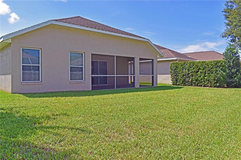 The exterior of a tan house features a screened-in patio and a large grassy backyard — 14499 TAMARIND LOOP, SPRING HILL, FL