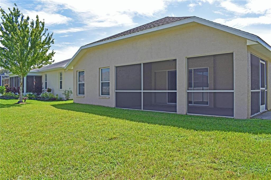 The exterior of a beige house features a screened-in porch and a large grassy yard — 14499 TAMARIND LOOP, SPRING HILL, FL