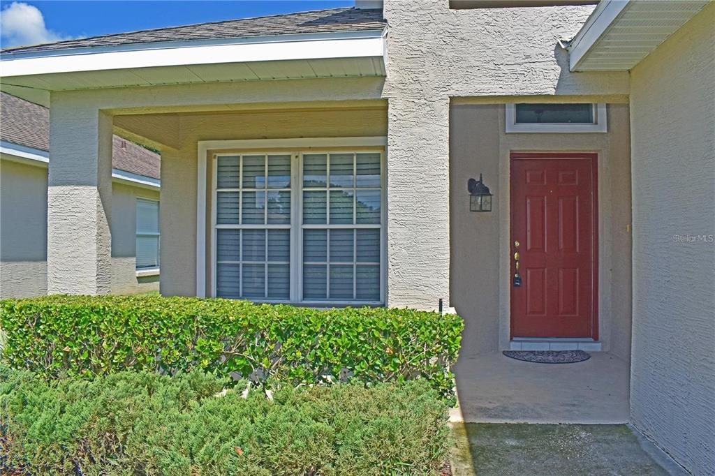 A red front door is set into a stucco house exterior with a covered porch — 14499 TAMARIND LOOP, SPRING HILL, FL
