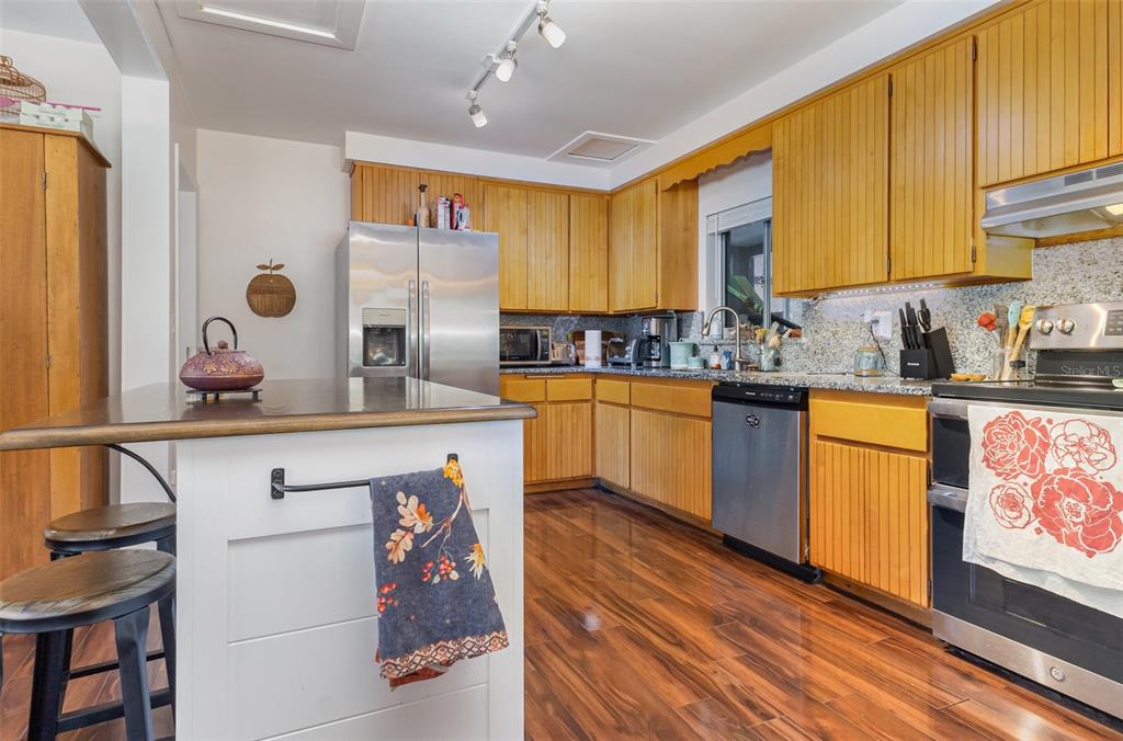 A kitchen features wood cabinets, stainless steel appliances, granite countertops, and a white island — 29 GOLF VIEW CIRCLE NE, WINTER HAVEN, FL