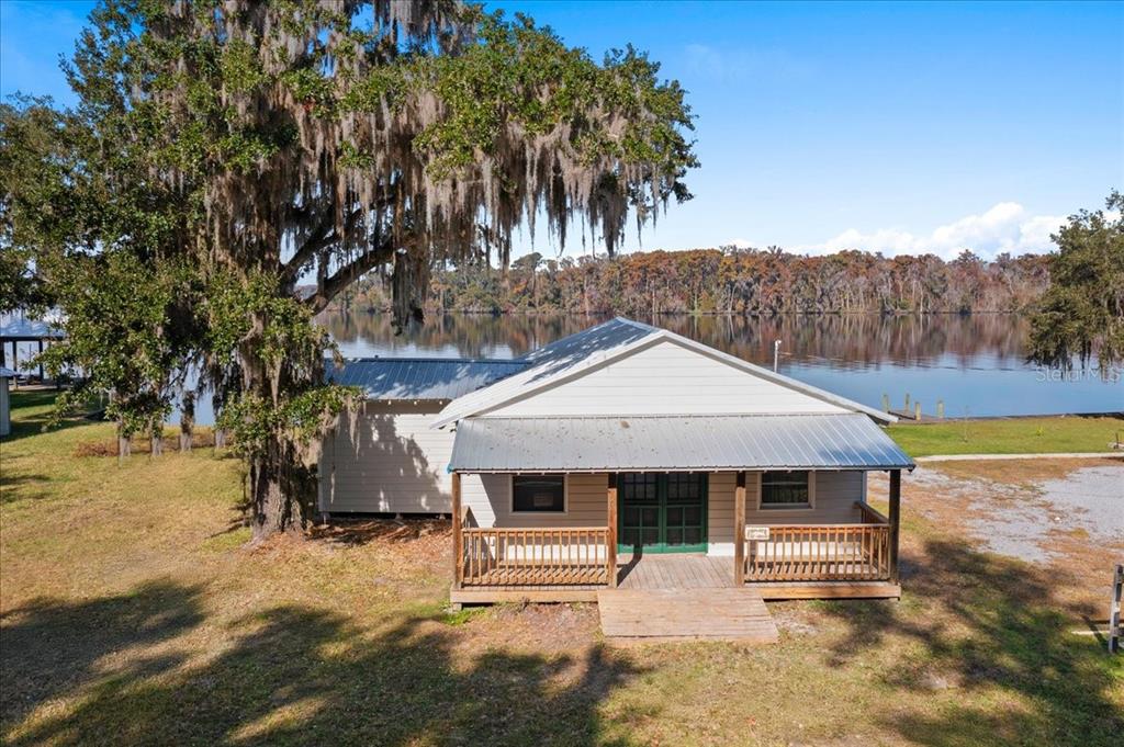 A single-story house with a metal roof and front porch sits beside a calm lake — 13555 COUNTY ROAD 13, ST AUGUSTINE, FL
