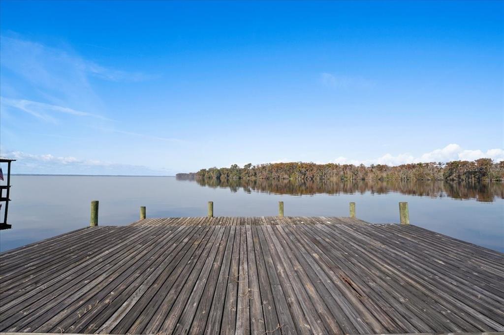 A wooden dock extends over a calm lake toward a tree-lined shore under a blue sky — 13555 COUNTY ROAD 13, ST AUGUSTINE, FL