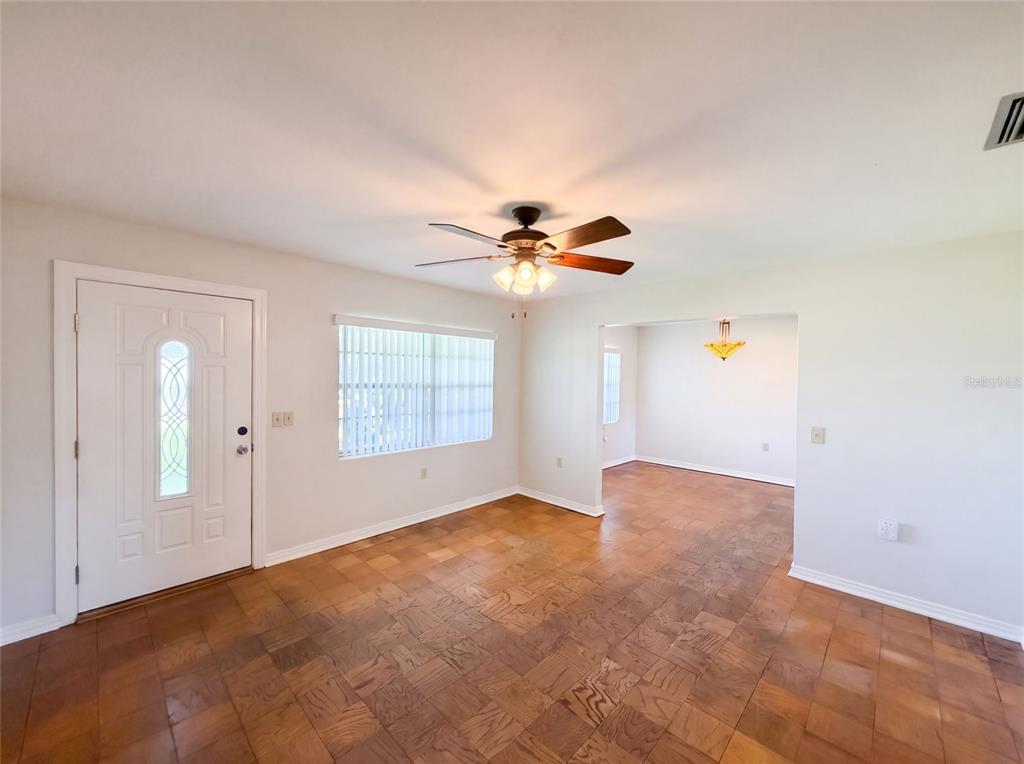 A room with parquet wood flooring, a ceiling fan, a white front door, and windows — 1305 W SPENCER STREET, PLANT CITY, FL