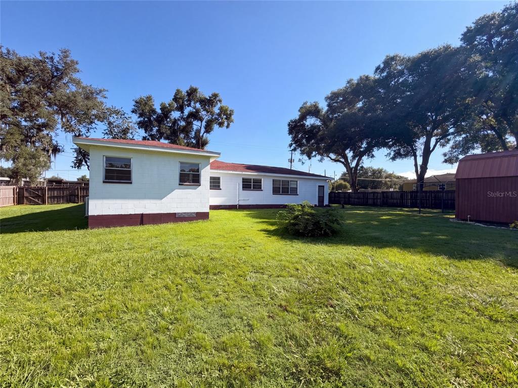 The backyard of a white house features a lawn, trees, and a small storage shed — 1305 W SPENCER STREET, PLANT CITY, FL