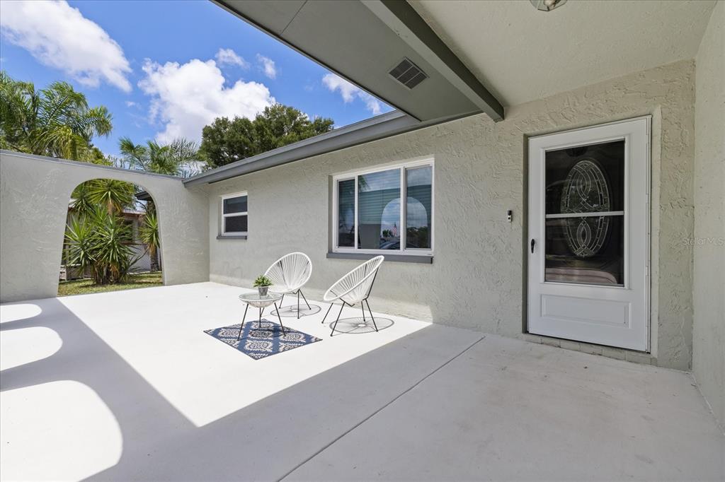 A covered patio features white stucco walls, two modern chairs, and an arched entryway — 5865 TERN DRIVE, NEW PORT RICHEY, FL