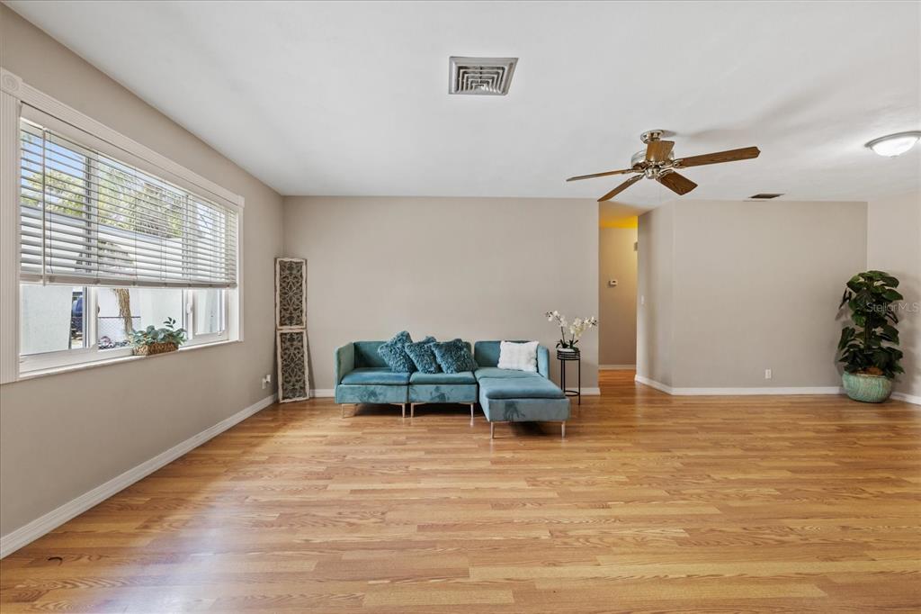 A living room with hardwood floors, a teal sectional sofa, and a ceiling fan — 5865 TERN DRIVE, NEW PORT RICHEY, FL