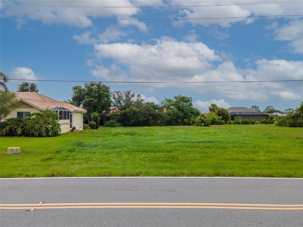 A vacant, grassy lot sits between two houses along a paved road under a cloudy sky — 4200 CAPE HAZE DRIVE, PLACIDA, FL
