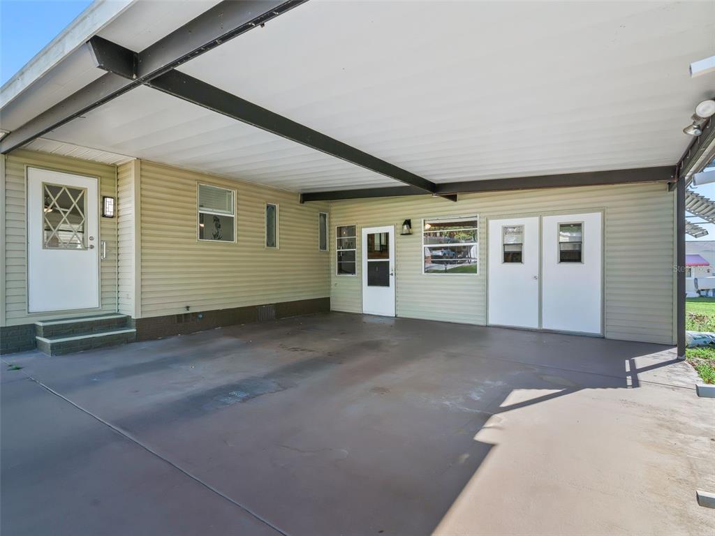 A covered concrete carport features light green siding, several white doors, and dark structural beams — 1514 HILLCREST DRIVE, LADY LAKE, FL