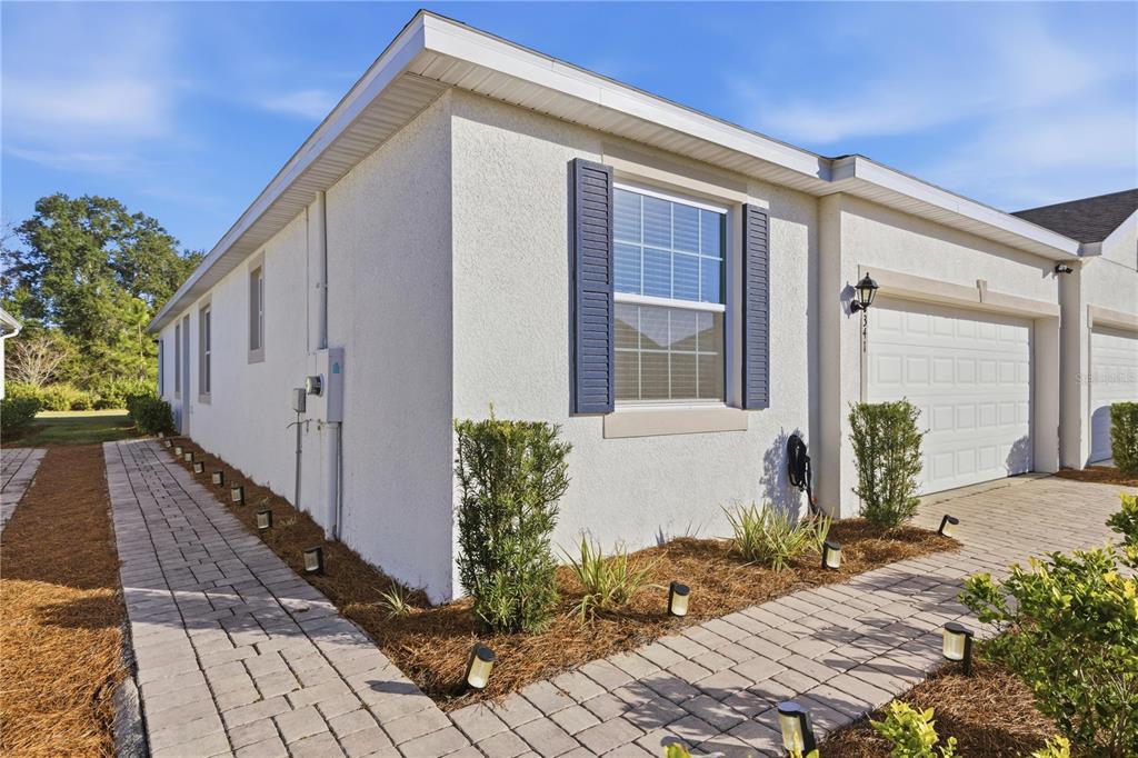 A side view of a white stucco house with a paved walkway and garage — 5341 NW 48TH PLACE, OCALA, FL