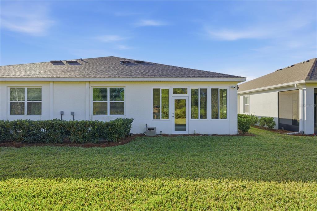 The rear exterior of a white stucco house features a glass-enclosed patio and lawn — 5341 NW 48TH PLACE, OCALA, FL