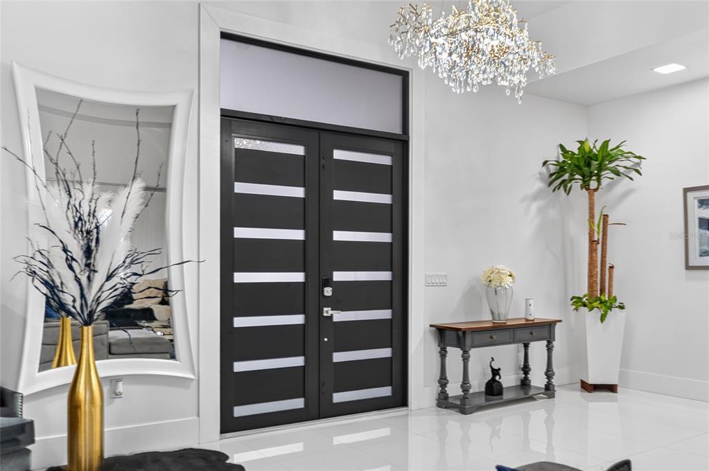 A modern entryway features double black doors, a crystal chandelier, and a white console table — 20722 QUINELLA STREET, ORLANDO, FL