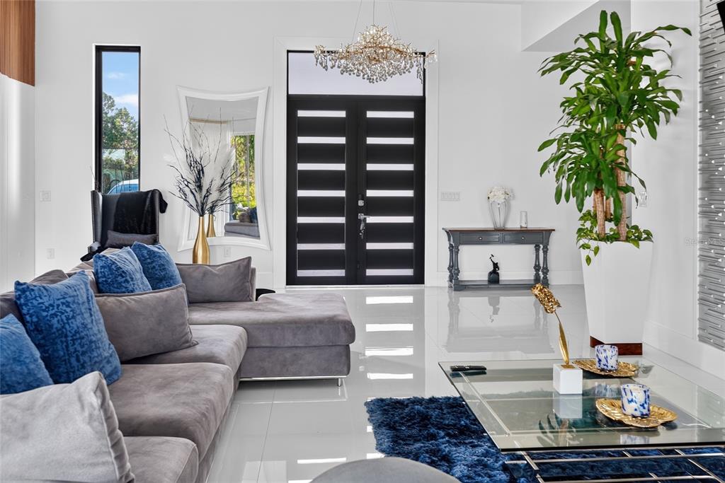 A modern living room features a grey sectional sofa, a glass coffee table, and double doors — 20722 QUINELLA STREET, ORLANDO, FL