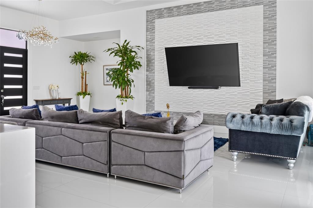 A modern living room features a large gray sectional sofa, a tufted armchair, and a television — 20722 QUINELLA STREET, ORLANDO, FL