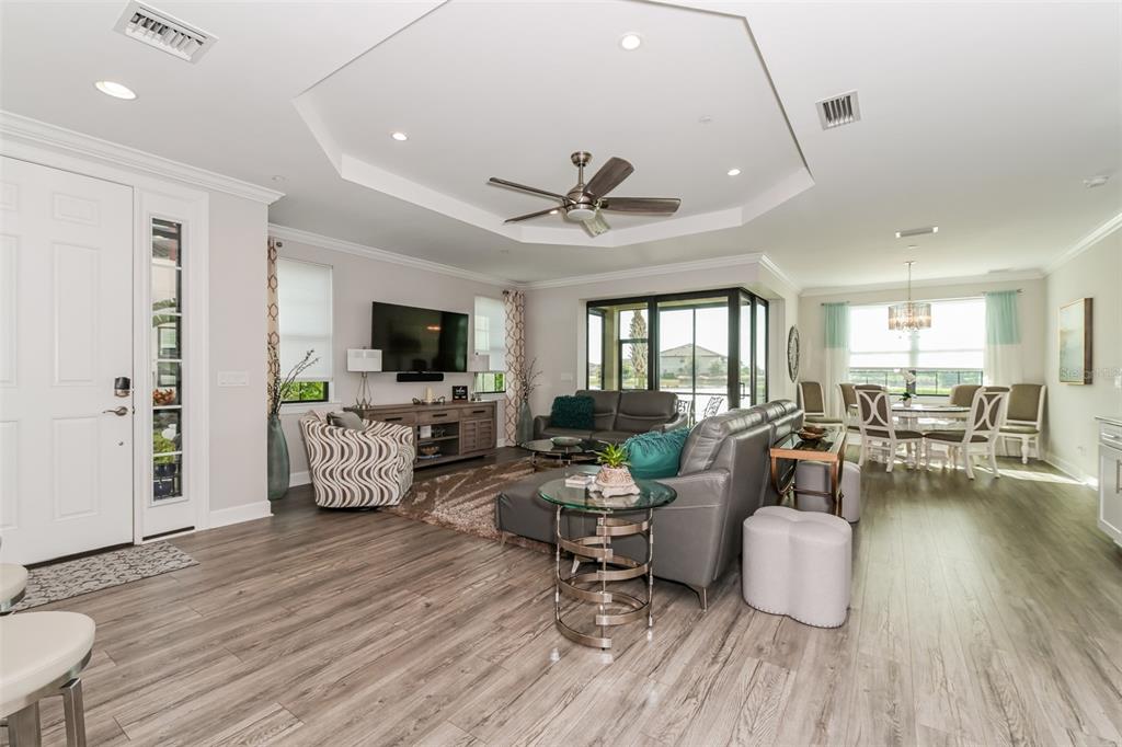 A living room with wood-look flooring, a tray ceiling, and an adjacent dining area — 9636 MONTELANICO LOOP UNIT 101, NAPLES, FL