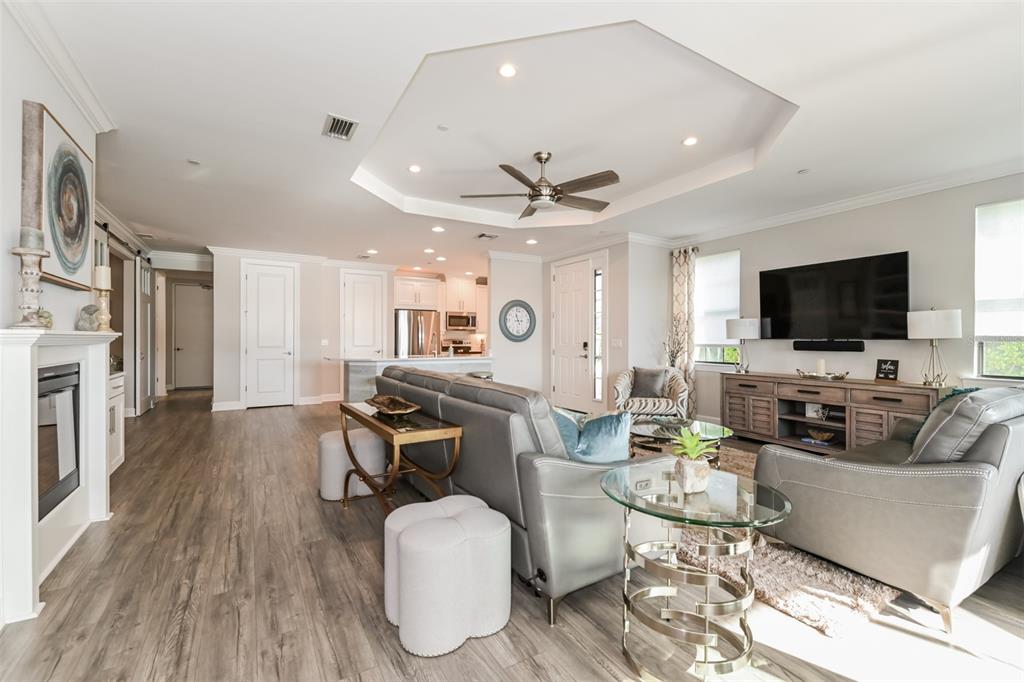 An open-concept living room features a tray ceiling, gray leather furniture, and wood-look flooring — 9636 MONTELANICO LOOP UNIT 101, NAPLES, FL