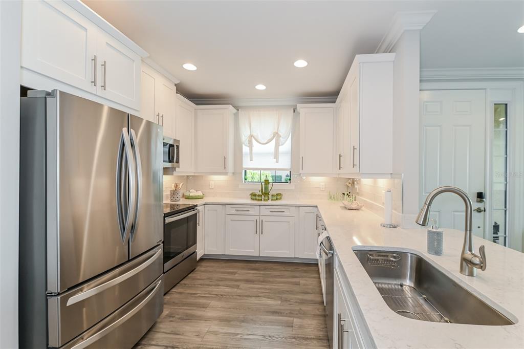 A modern kitchen features white cabinets, stainless steel appliances, and a quartz-topped island with sink — 9636 MONTELANICO LOOP UNIT 101, NAPLES, FL