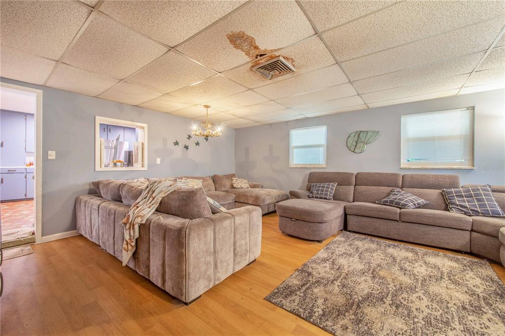 A living room features light blue walls, wood-look flooring, two large sectionals, and a water-damaged ceiling — 308 GRANADA ROAD, AUBURNDALE, FL