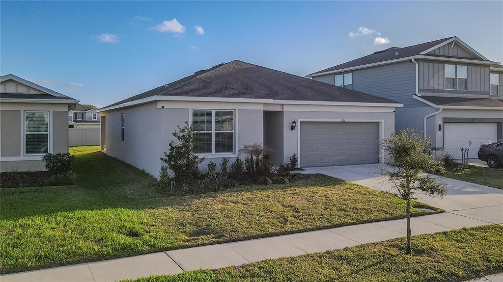A single-story suburban house with a gray stucco exterior, a two-car garage, and a lawn — 1821 GROVELINE ROAD, ST CLOUD, FL