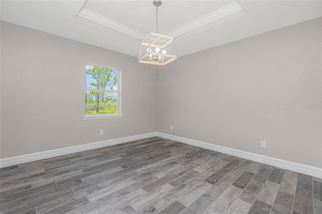 An empty room features gray walls, wood-look tile flooring, a tray ceiling, and a chandelier — 6 BULK COURT, PLACIDA, FL