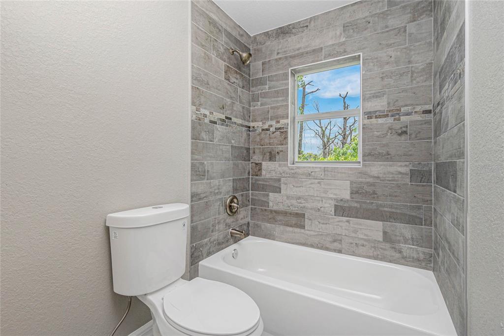 A bathroom features a white toilet, a white bathtub, and gray wood-look tile walls — 6 BULK COURT, PLACIDA, FL