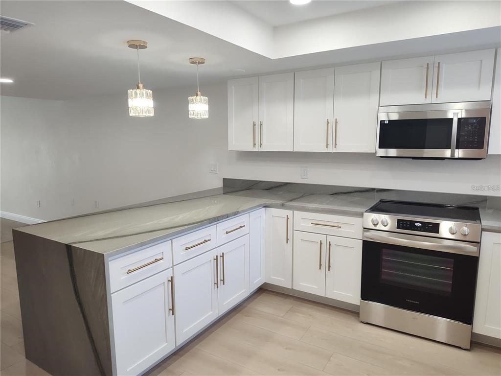 A modern kitchen features white cabinetry, stainless steel appliances, and a large gray-veined island — 255 CAPRI CIRCLE N UNIT 36, TREASURE ISLAND, FL